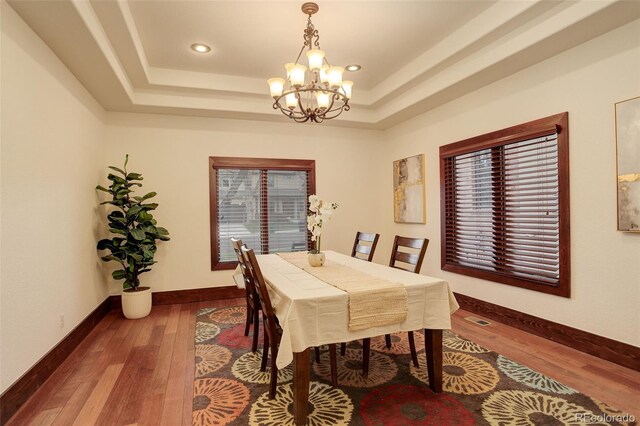 dining space with an inviting chandelier, wood-type flooring, visible vents, baseboards, and a tray ceiling