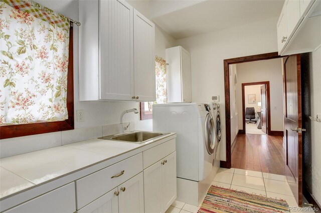 clothes washing area with a sink, light wood-type flooring, cabinet space, and washer and clothes dryer