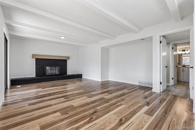 7351 S Marion St, Centennial, CO 80122 - unfurnished living room featuring beamed ceiling, wood finished floors, and a brick fireplace