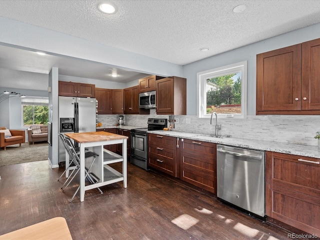 966 Cherry Blossom Ct, Highlands Ranch, CO 80126 - kitchen featuring appliances with stainless steel finishes, dark wood-style flooring, decorative backsplash, a textured ceiling, and light stone countertops