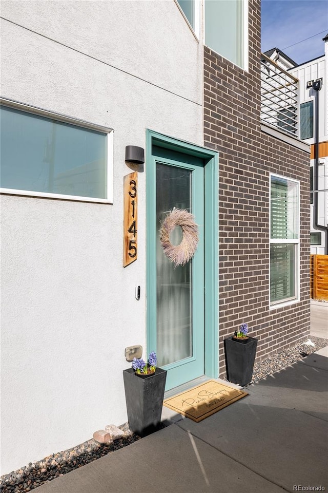 view of exterior entry featuring stucco siding and brick siding