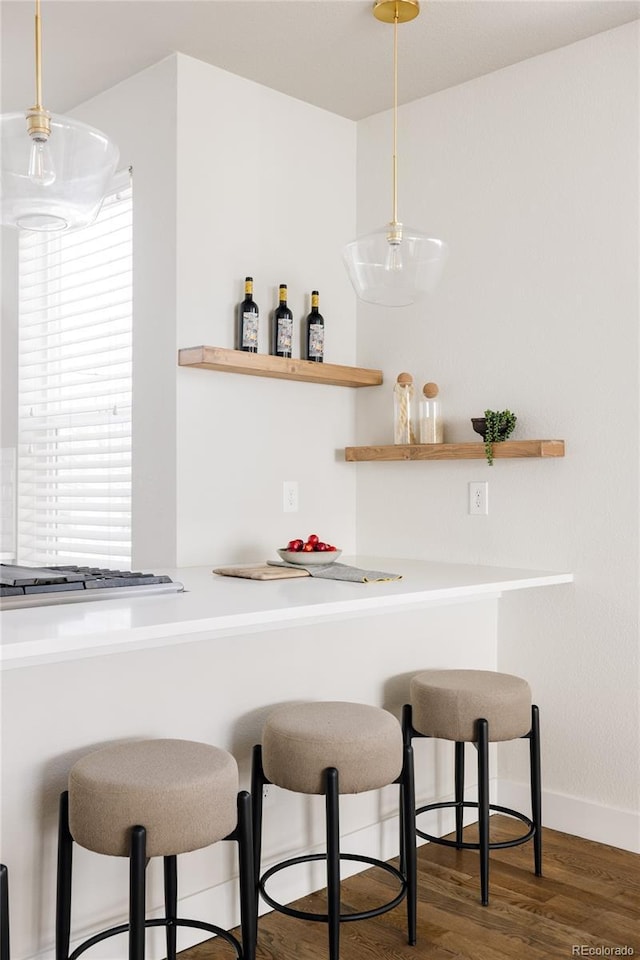 bar featuring baseboards, stainless steel gas cooktop, a dry bar, wood finished floors, and hanging light fixtures