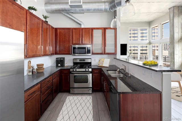 kitchen with light hardwood / wood-style floors, sink, kitchen peninsula, appliances with stainless steel finishes, and dark stone countertops