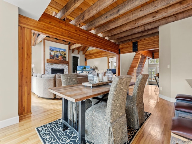 dining area with a fireplace, beamed ceiling, wood ceiling, and light wood-type flooring