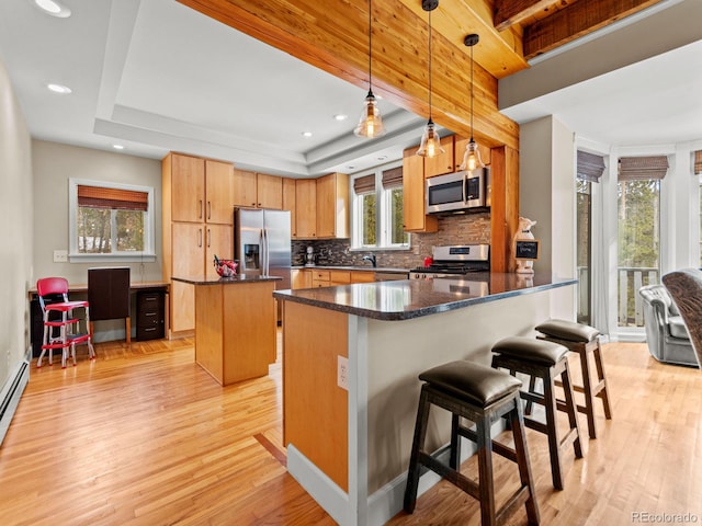 kitchen with pendant lighting, dark stone countertops, light wood-type flooring, appliances with stainless steel finishes, and a kitchen island