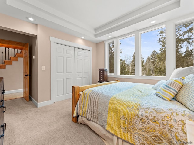 bedroom with a tray ceiling, light carpet, and a closet