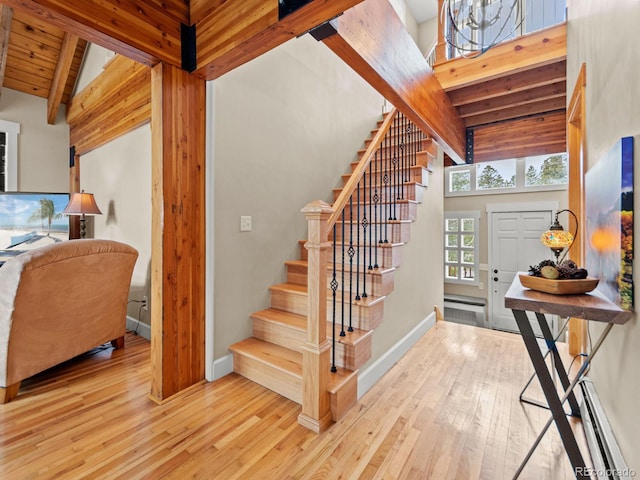 staircase with a towering ceiling, a baseboard heating unit, and hardwood / wood-style flooring