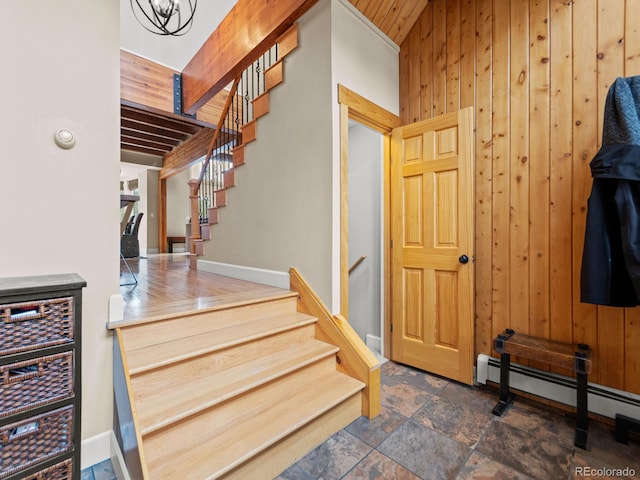 staircase with a chandelier, wood walls, beamed ceiling, and a baseboard radiator