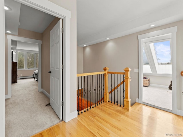 hallway featuring a skylight, plenty of natural light, a baseboard heating unit, and hardwood / wood-style flooring