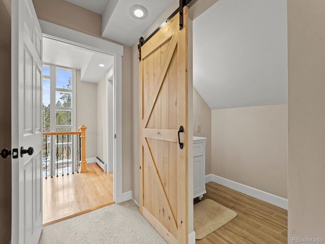 hallway with light wood-type flooring, a barn door, and baseboard heating