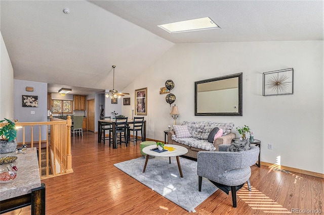 living area featuring vaulted ceiling with skylight, ceiling fan, baseboards, and wood finished floors