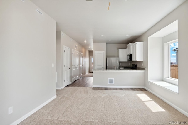 kitchen with kitchen peninsula, carpet, stainless steel appliances, ceiling fan, and white cabinetry