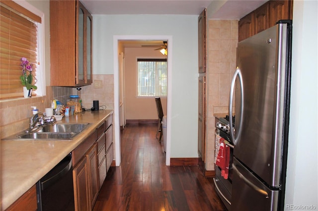 kitchen featuring appliances with stainless steel finishes, a sink, brown cabinetry, and glass insert cabinets