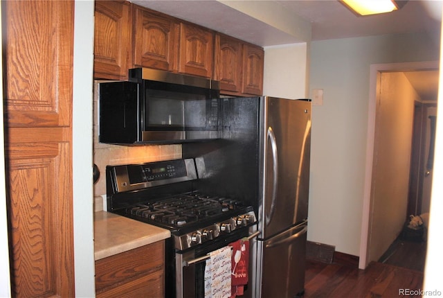 kitchen featuring gas stove, brown cabinetry, light countertops, and dark wood-style flooring