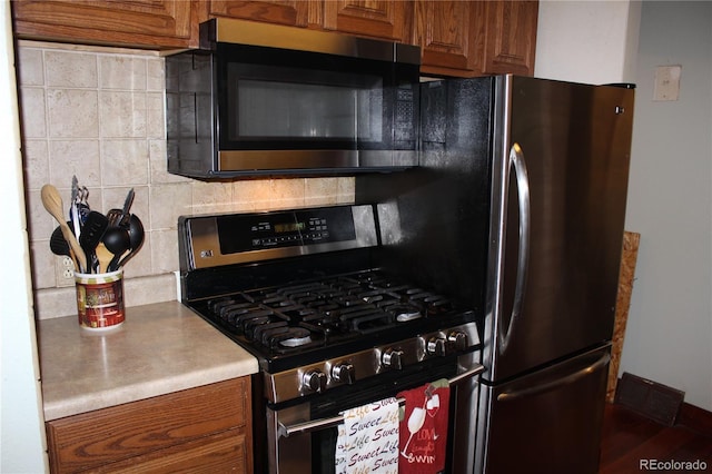 kitchen with appliances with stainless steel finishes, brown cabinetry, and tasteful backsplash