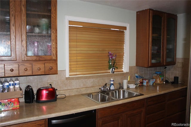 kitchen with black dishwasher, a sink, light countertops, decorative backsplash, and glass insert cabinets