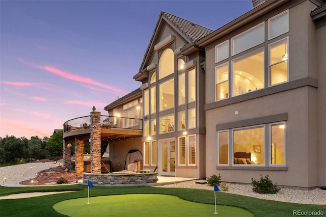 back house at dusk with a patio, a balcony, and an outdoor stone fireplace