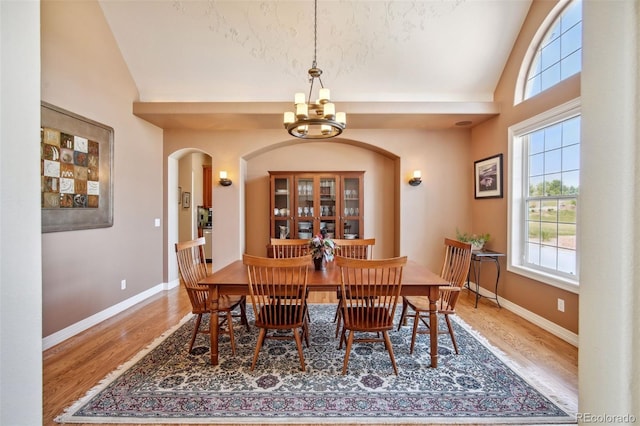 dining area featuring high vaulted ceiling, hardwood / wood-style floors, and a notable chandelier