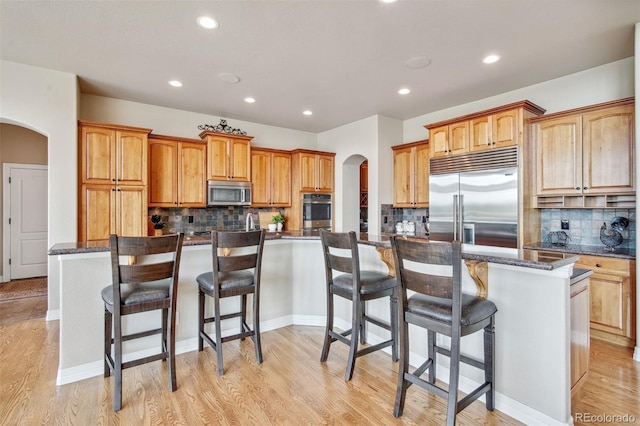 kitchen with a kitchen island, a breakfast bar area, backsplash, stainless steel appliances, and light wood-type flooring