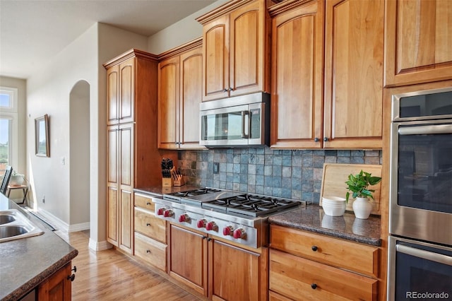 kitchen featuring light wood-type flooring, appliances with stainless steel finishes, backsplash, and dark stone counters