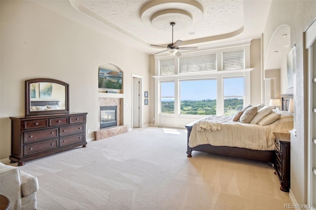 bedroom featuring a raised ceiling, a high end fireplace, a high ceiling, light carpet, and ceiling fan