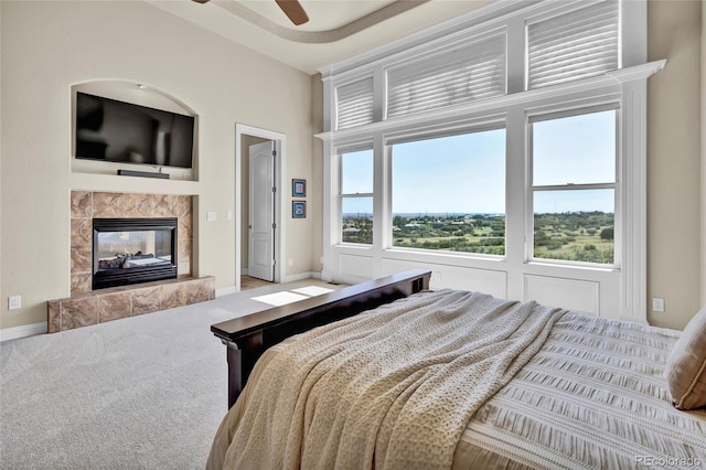 bedroom featuring ceiling fan, a tiled fireplace, and carpet