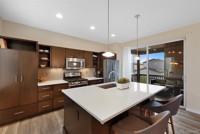 kitchen featuring open shelves, appliances with stainless steel finishes, a breakfast bar, a sink, and an island with sink