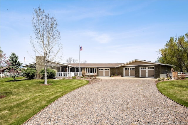 single story home featuring an attached garage, a front lawn, brick siding, a sunroom, and gravel driveway