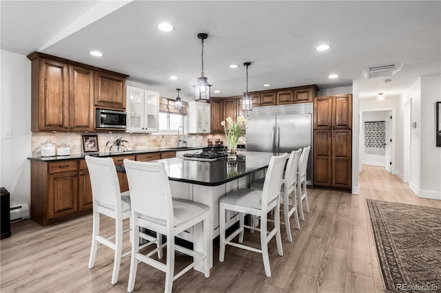 kitchen with built in appliances, a baseboard heating unit, dark countertops, and a kitchen bar
