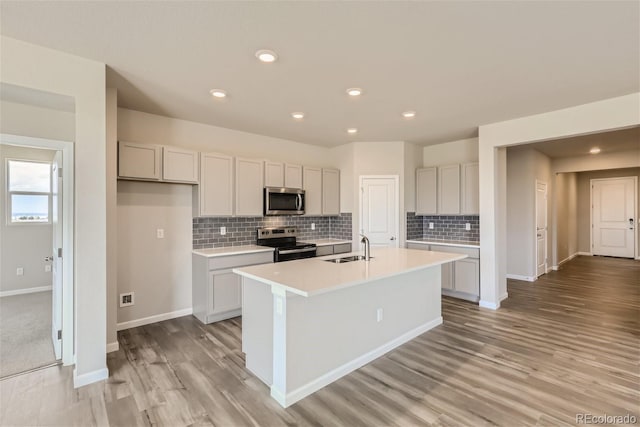 kitchen featuring backsplash, stainless steel appliances, light hardwood / wood-style flooring, a center island with sink, and sink