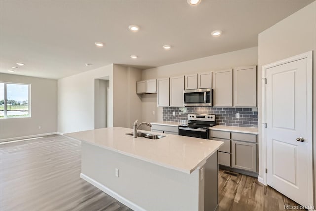 kitchen featuring appliances with stainless steel finishes, light hardwood / wood-style floors, sink, and an island with sink