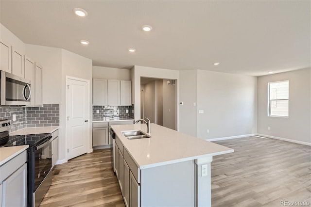 kitchen featuring a center island with sink, stainless steel appliances, sink, and light hardwood / wood-style flooring