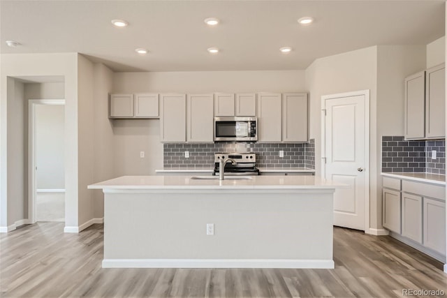 kitchen with stainless steel appliances, light hardwood / wood-style floors, a center island with sink, and sink