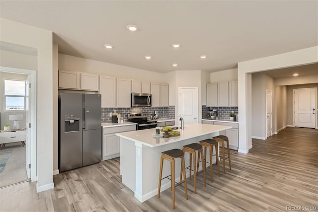 kitchen with decorative backsplash, stainless steel appliances, light hardwood / wood-style floors, and a center island with sink