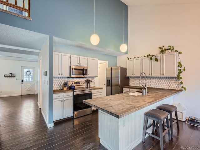 kitchen featuring kitchen peninsula, appliances with stainless steel finishes, dark hardwood / wood-style flooring, decorative light fixtures, and white cabinetry