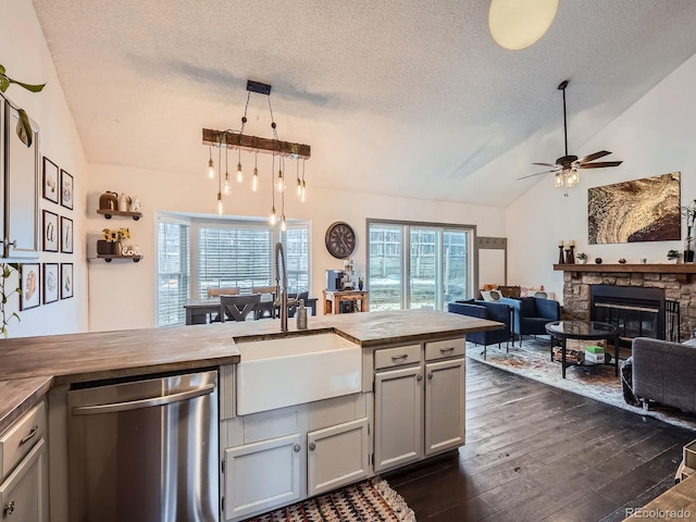 kitchen with stainless steel dishwasher, vaulted ceiling, dark wood-type flooring, sink, and a stone fireplace