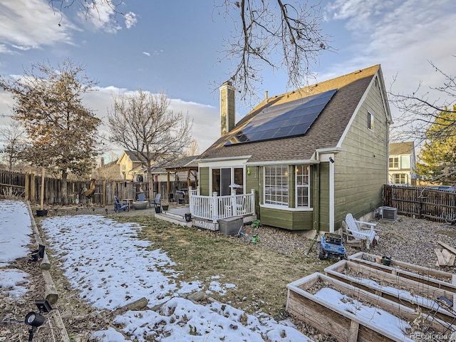 snow covered house with cooling unit, a deck, and solar panels