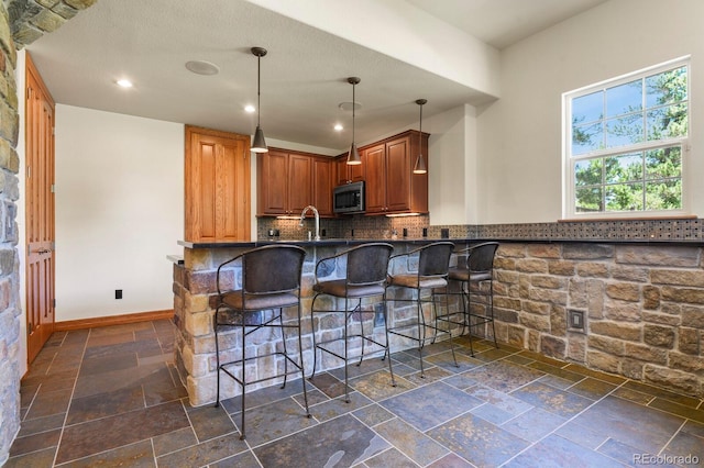 11268 Bell Cross Cir, Parker, CO 80138 - kitchen featuring stone tile floors, stainless steel microwave, dark countertops, tasteful backsplash, and a kitchen bar