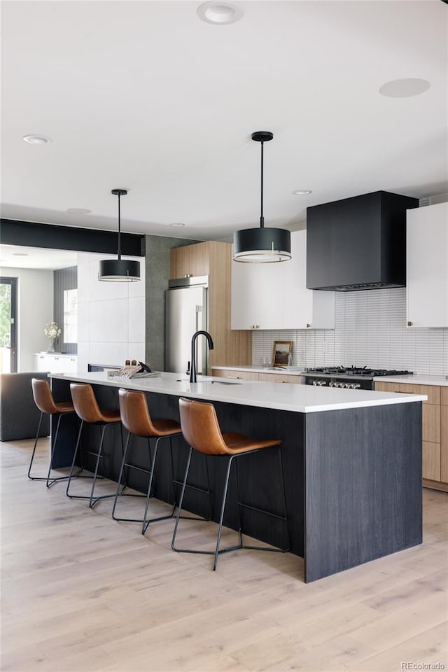 kitchen with a spacious island, hanging light fixtures, wall chimney exhaust hood, light wood-type flooring, and fridge