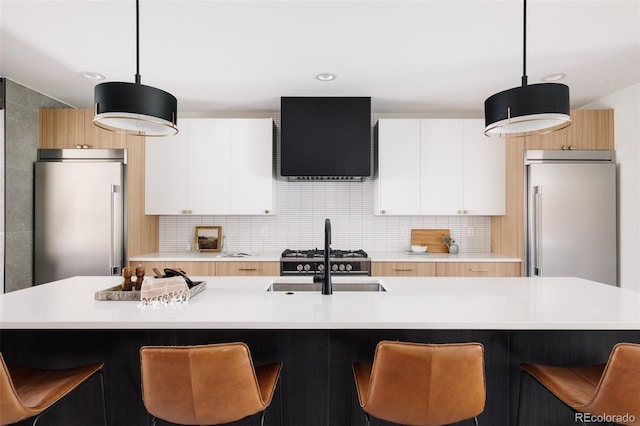 kitchen with a center island with sink, white cabinets, range hood, high quality fridge, and decorative light fixtures