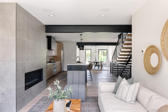 living room featuring beam ceiling, sink, hardwood / wood-style floors, a fireplace, and tile walls