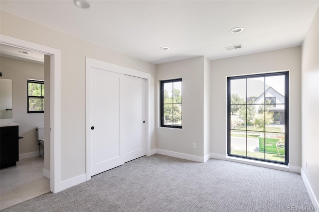 unfurnished bedroom with multiple windows, light carpet, and a closet