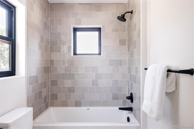 bathroom featuring tiled shower / bath combo, toilet, and a healthy amount of sunlight