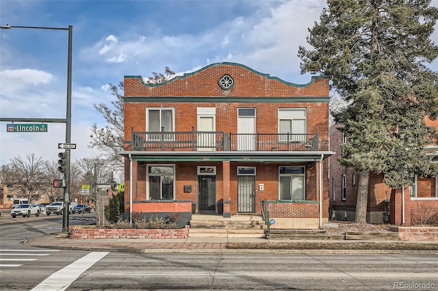 view of property with brick siding, a porch, and a balcony