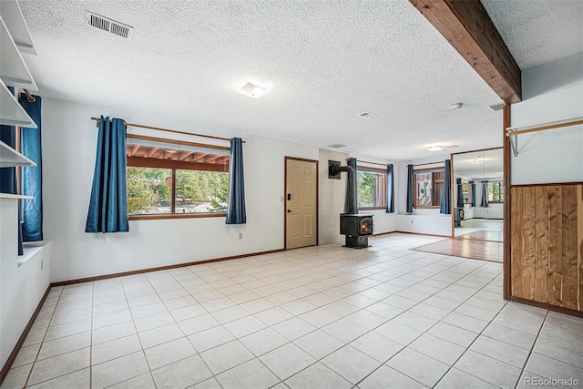 10858 Norton Ave, Conifer, CO 80433 - unfurnished room with light tile patterned floors, a textured ceiling, a wood stove, and visible vents