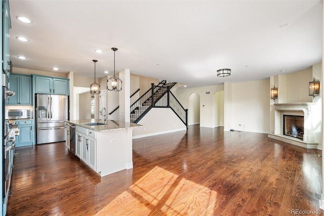 kitchen with a kitchen island with sink, dark wood-type flooring, sink, light stone countertops, and appliances with stainless steel finishes