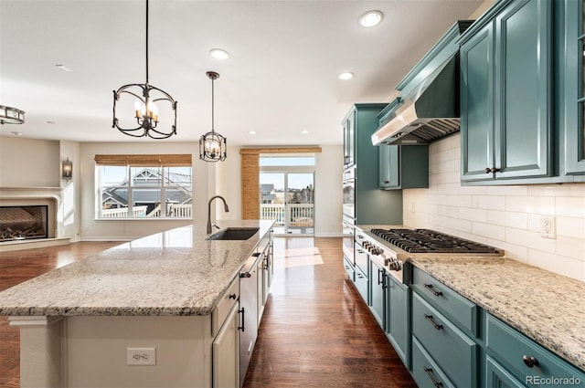 kitchen featuring dark wood-type flooring, sink, an island with sink, decorative light fixtures, and light stone counters