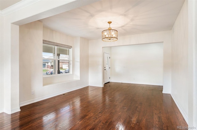 spare room with a notable chandelier and dark wood-type flooring