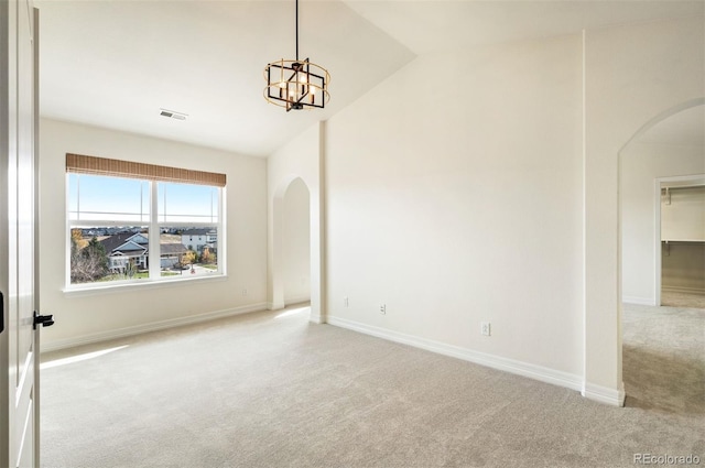 carpeted empty room with lofted ceiling and a chandelier