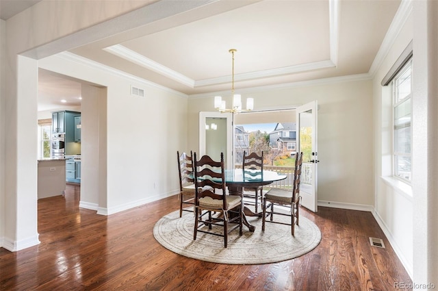 dining space featuring dark wood-type flooring, a raised ceiling, a healthy amount of sunlight, and a notable chandelier